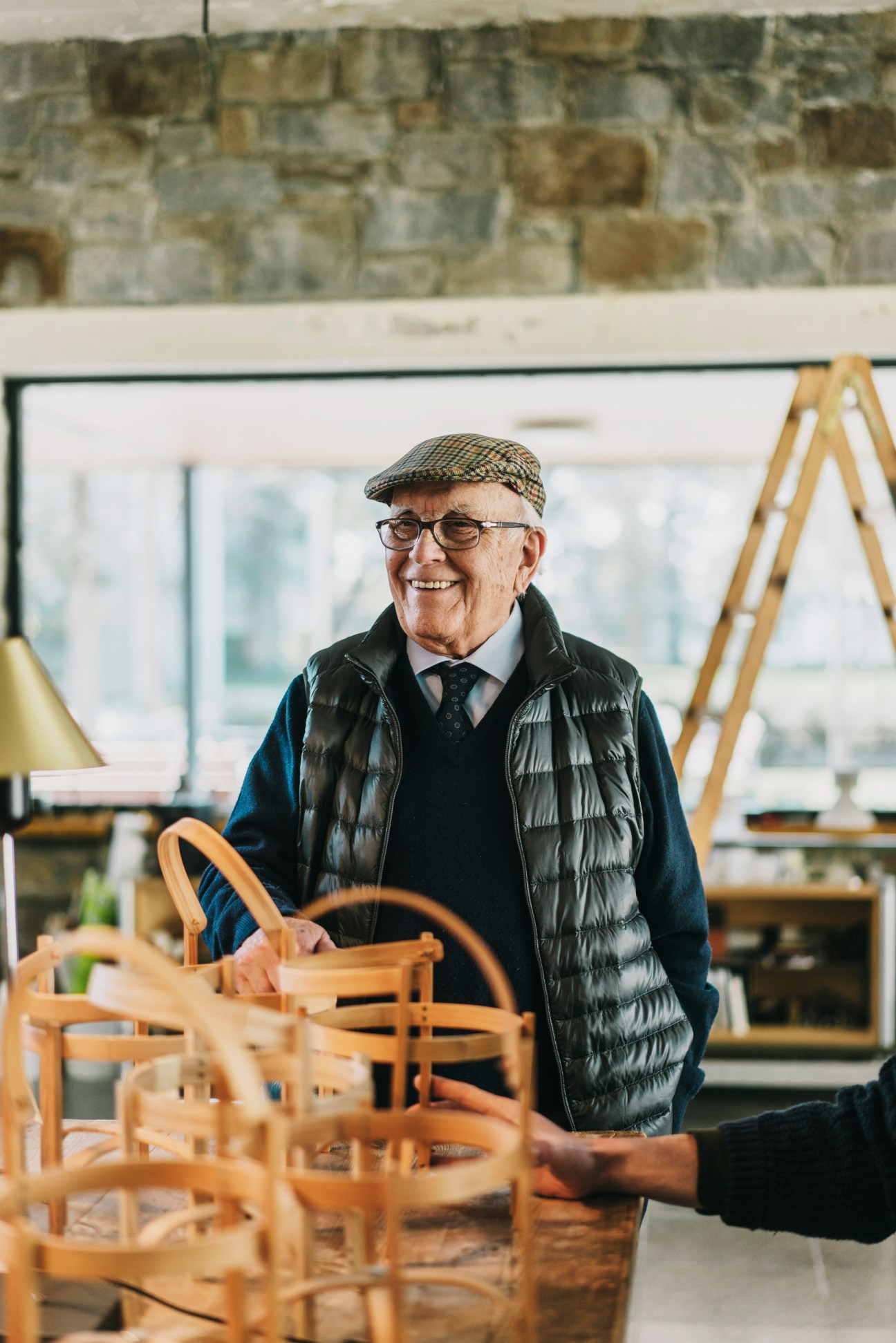 Industrial designer Miguel Milá smiles in his workshop surrounded by wooden chair prototypes.