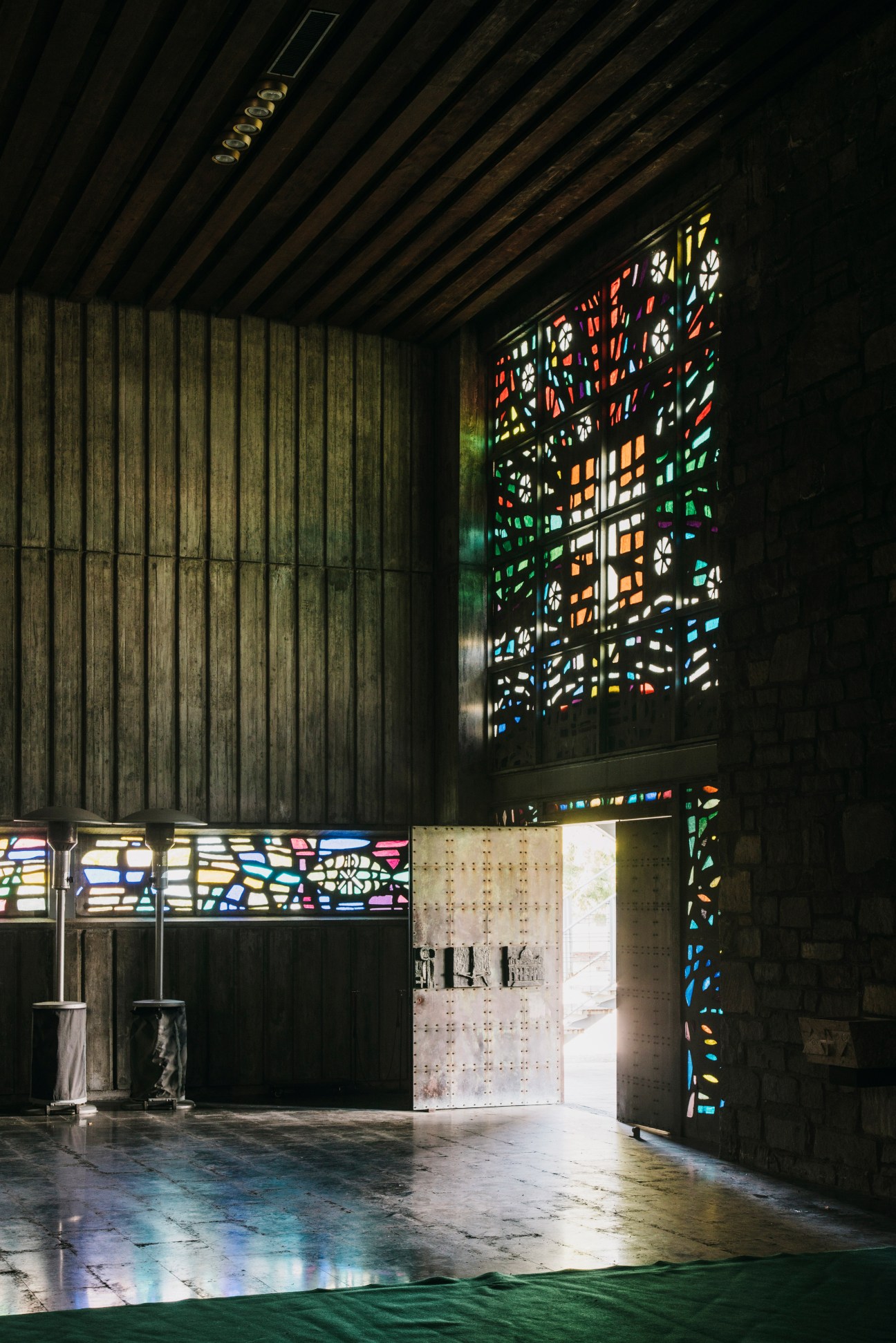 Colorful stained glass windows casting kaleidoscopic light patterns on wooden walls and floor in a chapel interior.