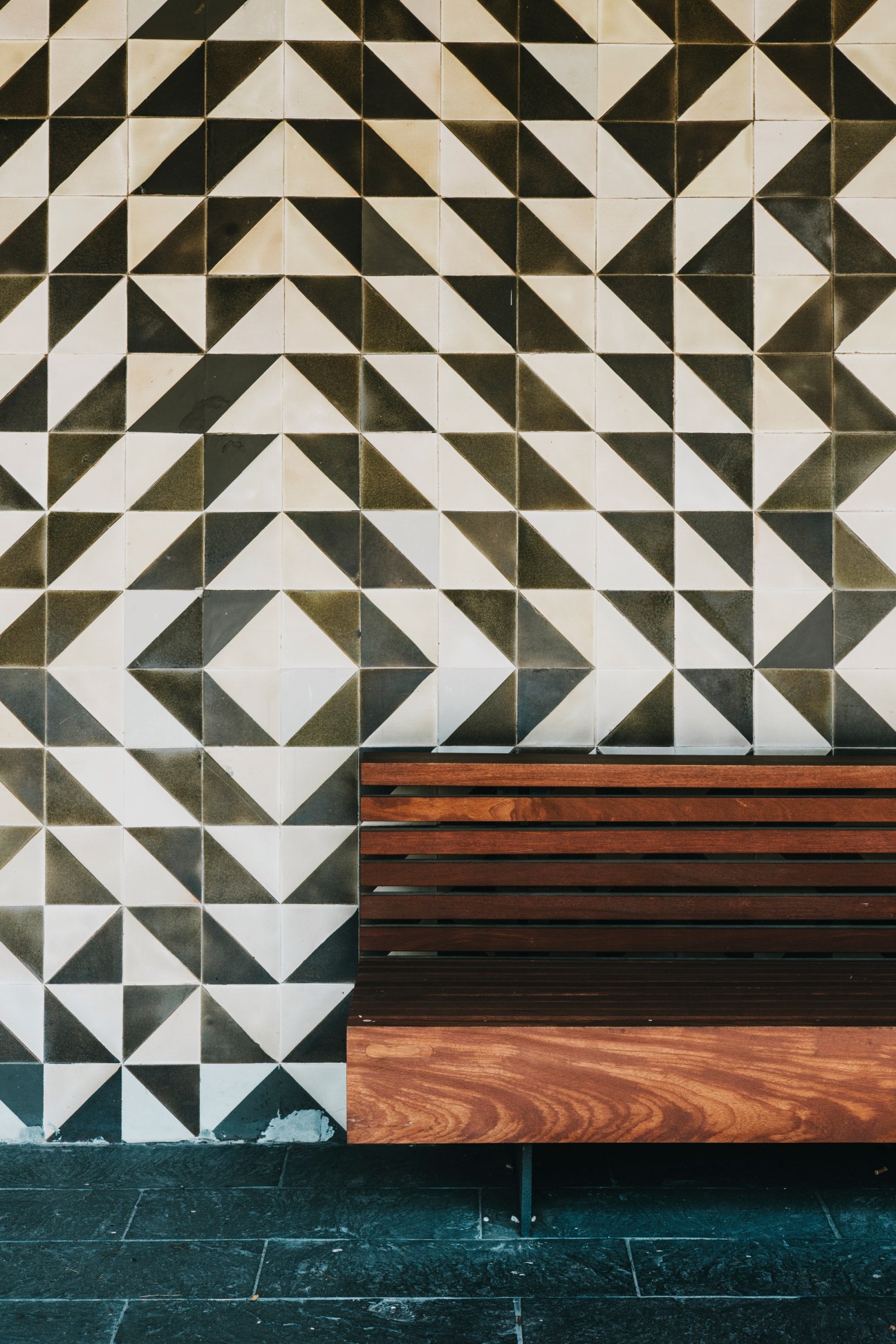 Moon bench with wooden slats against a geometric black and white ceramic tiled wall.