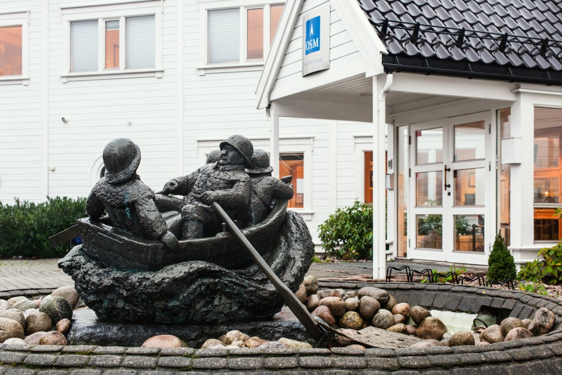 OSM Maritime Group headquarters building in Arendal with bronze seafaring sculpture in foreground.