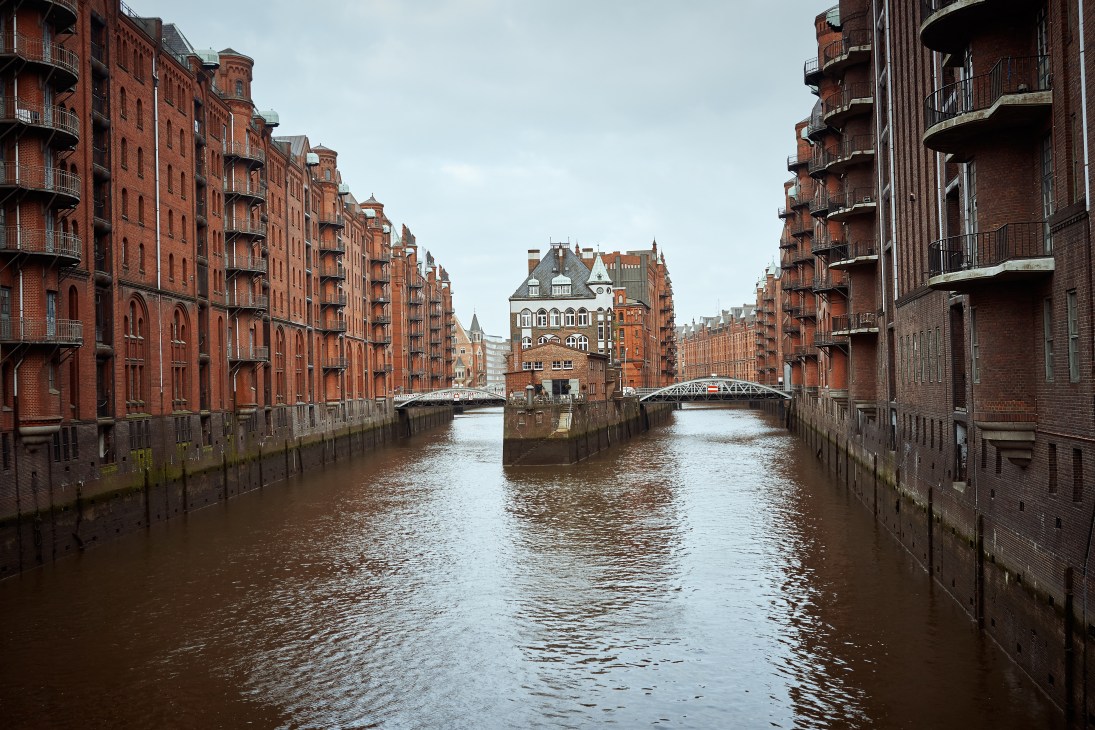 Historic red-brick waterfront buildings lining a calm canal in Hamburg's Speicherstadt district.