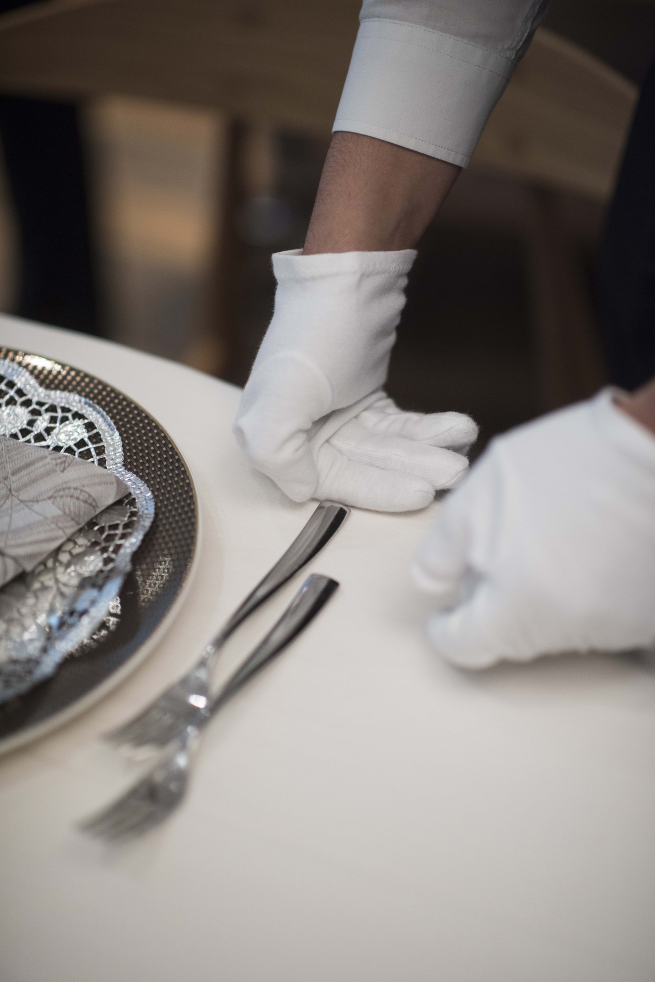 White-gloved server's hands checking cutlery placement beside an ornate plate during hospitality training.
