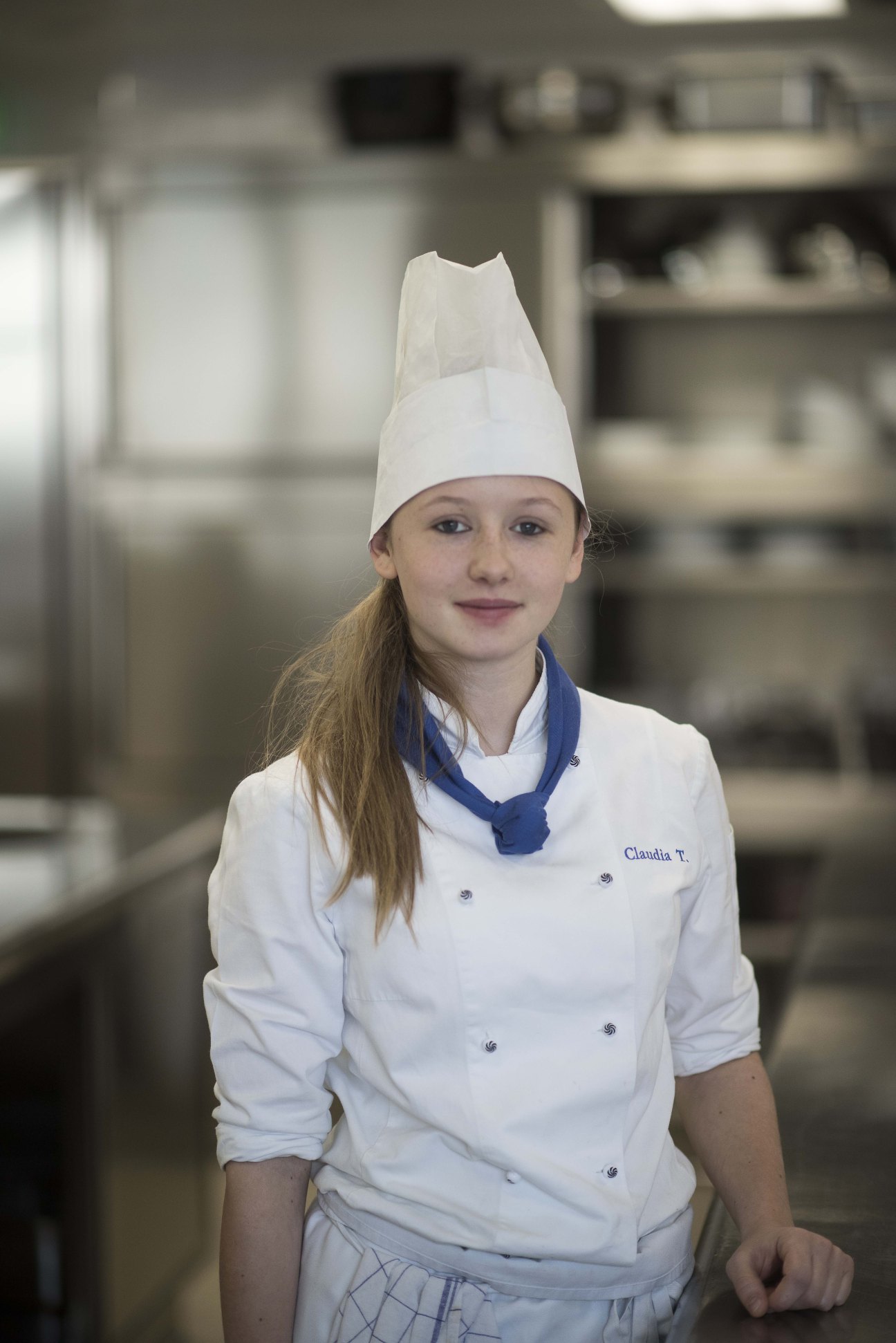 Student Claudia Troger wearing a white chef's coat and hat in a kitchen at Brunico Hotel School.