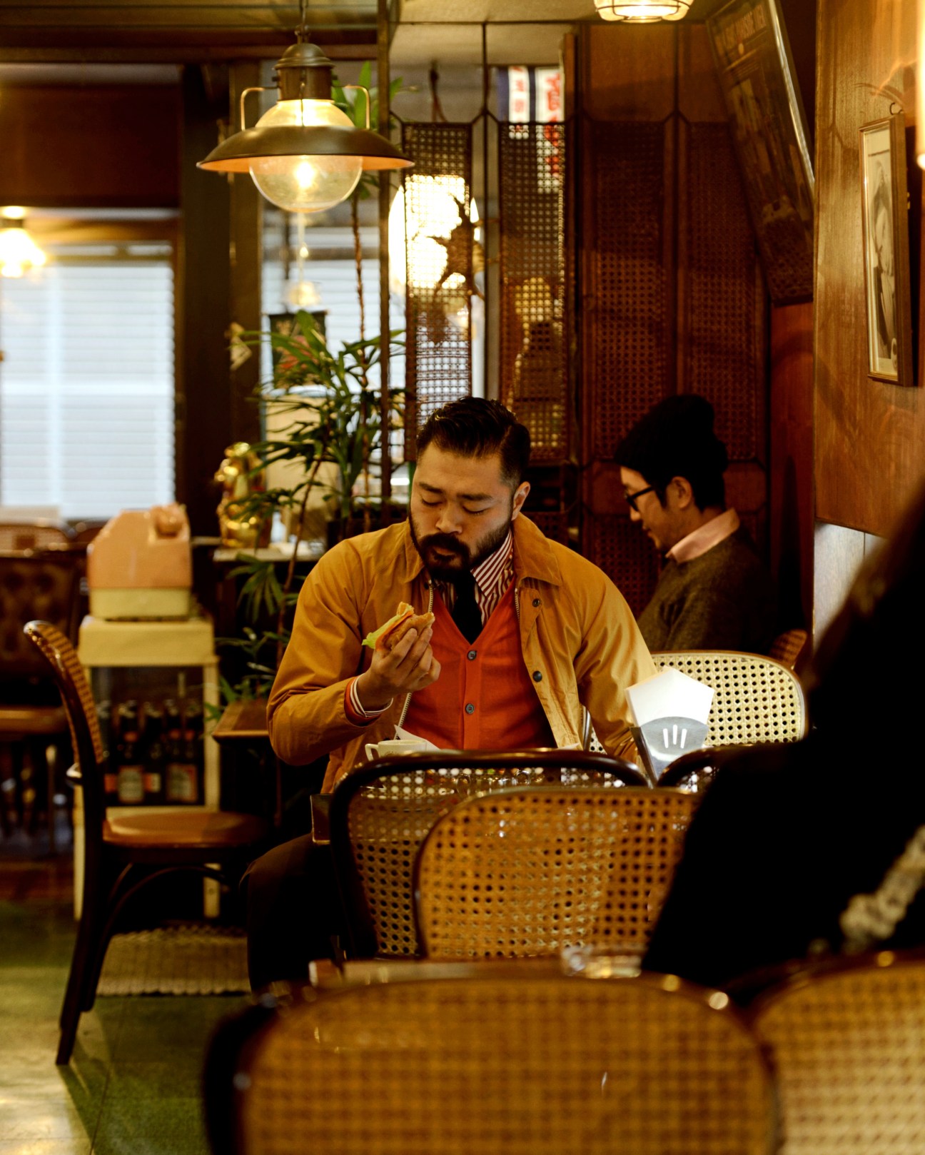 Man in Barbour jacket and Ermenegildo Zegna shirt eating a hot dog at Ginza Brazil café in Asakusa, Tokyo.