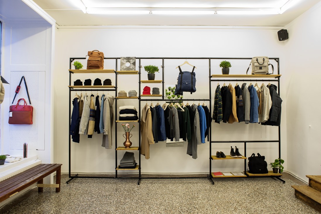 Interior of A Kind of Guise menswear store in Munich displaying clothing on metal racks with wooden shelves.