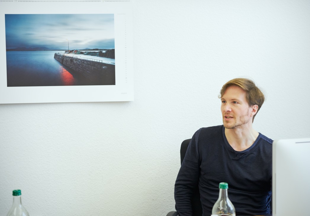 Dimitri Ladischensky, section editor covering Politics and Life, sitting in an office with maritime photography on the wall behind him.