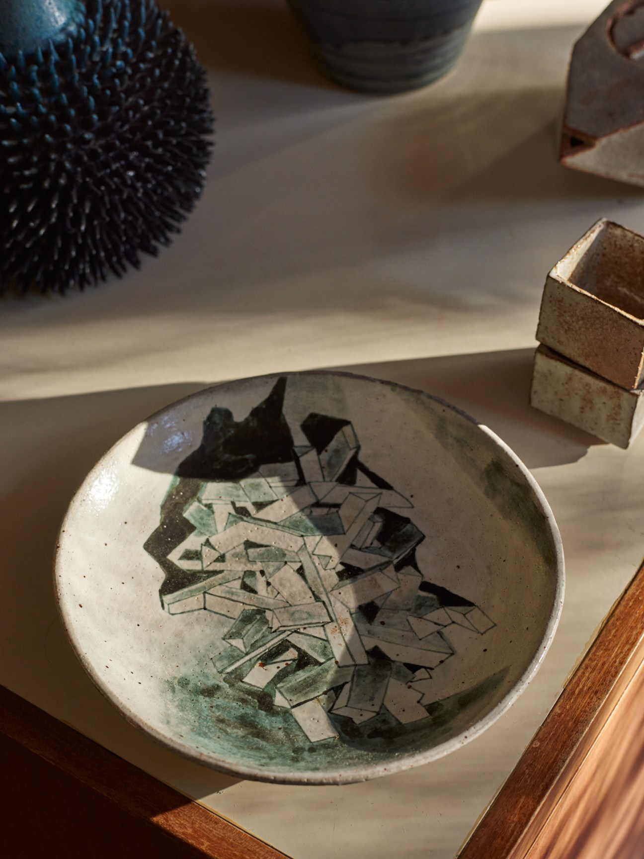 Painted earthenware plate by New Zealand artist Isobel Thom displayed among decorative objects.