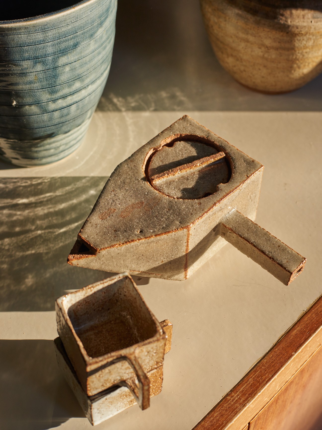 Earthenware teapot and cups by New Zealand artist Isobel Thom displayed on a light surface in sunlight.