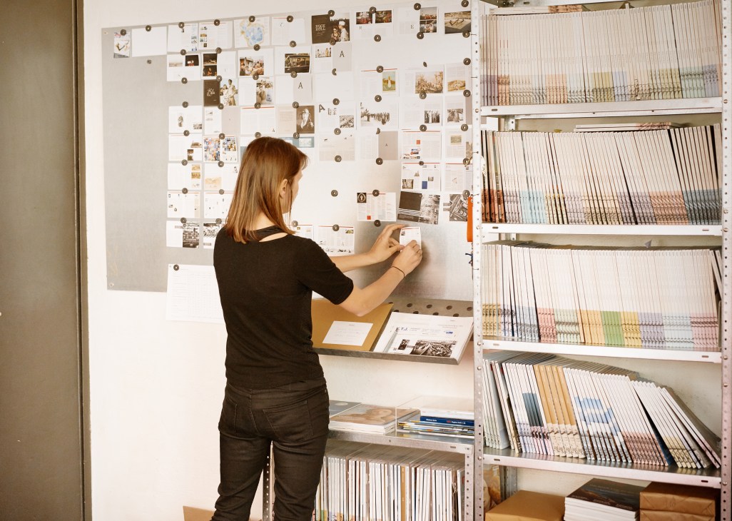 Woman pinning photographs and notes to a planning board in Mare magazine's office archive.