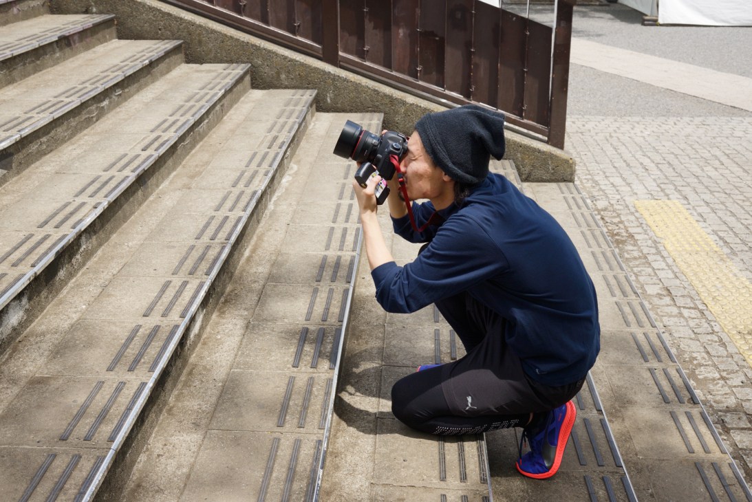 Photographer crouching on outdoor steps while shooting with a professional camera