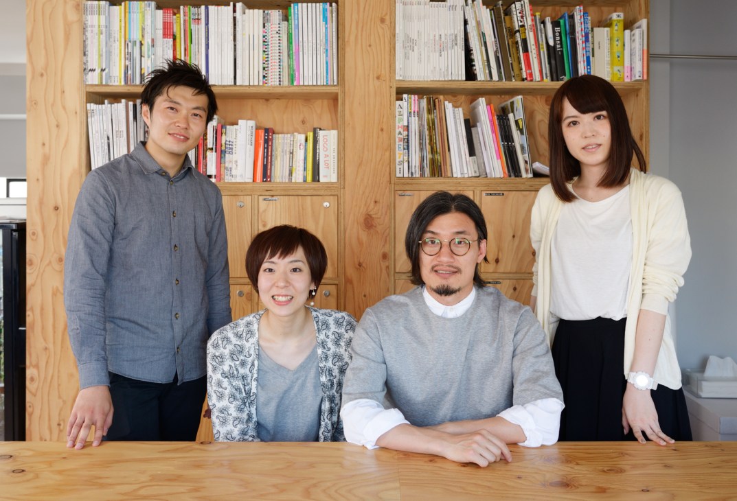 Four members of the Hashiruhito magazine team pose in front of wooden bookshelves filled with publications in their Tokyo office.