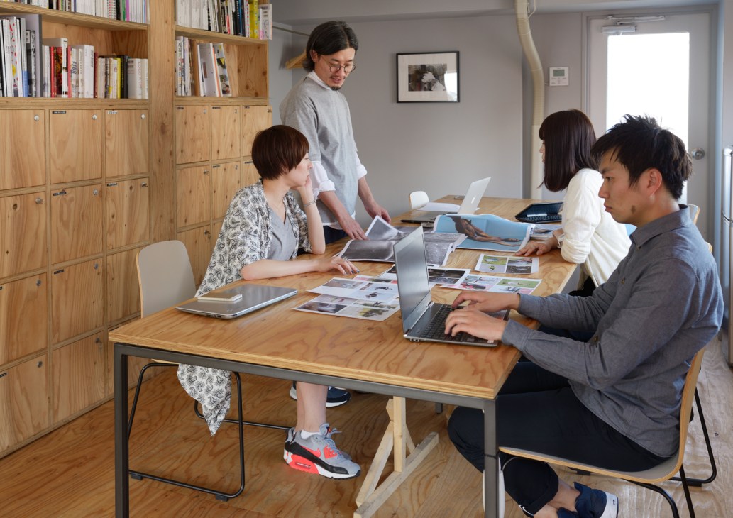 Hashiruhito editorial team collaborating at a wooden desk with laptops and printed materials in their Tokyo office.