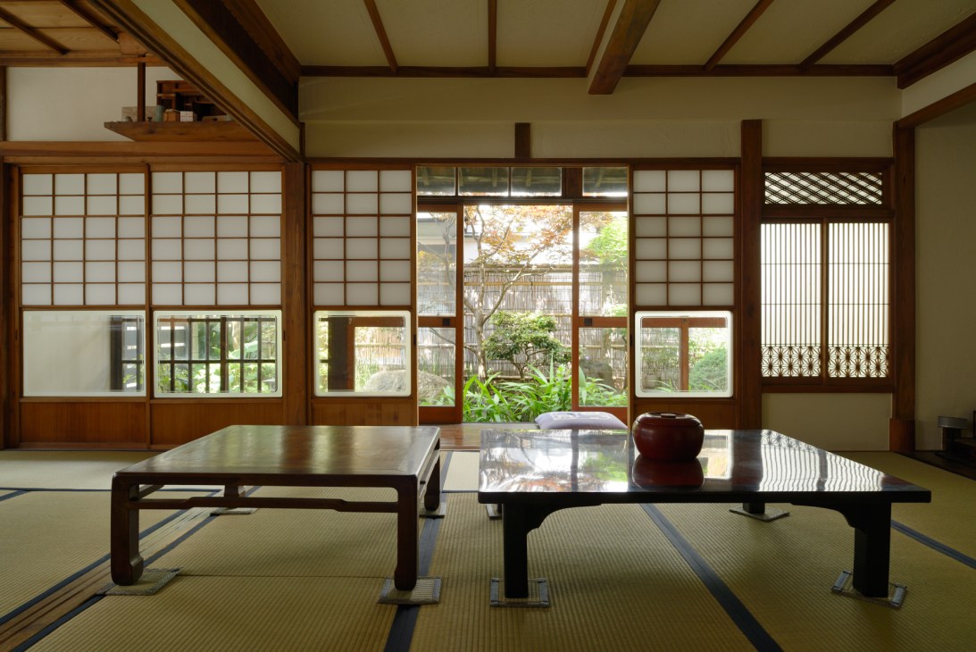 Japanese interior with tatami mats, wooden beams, fusuma sliding doors, and low tables overlooking a garden.