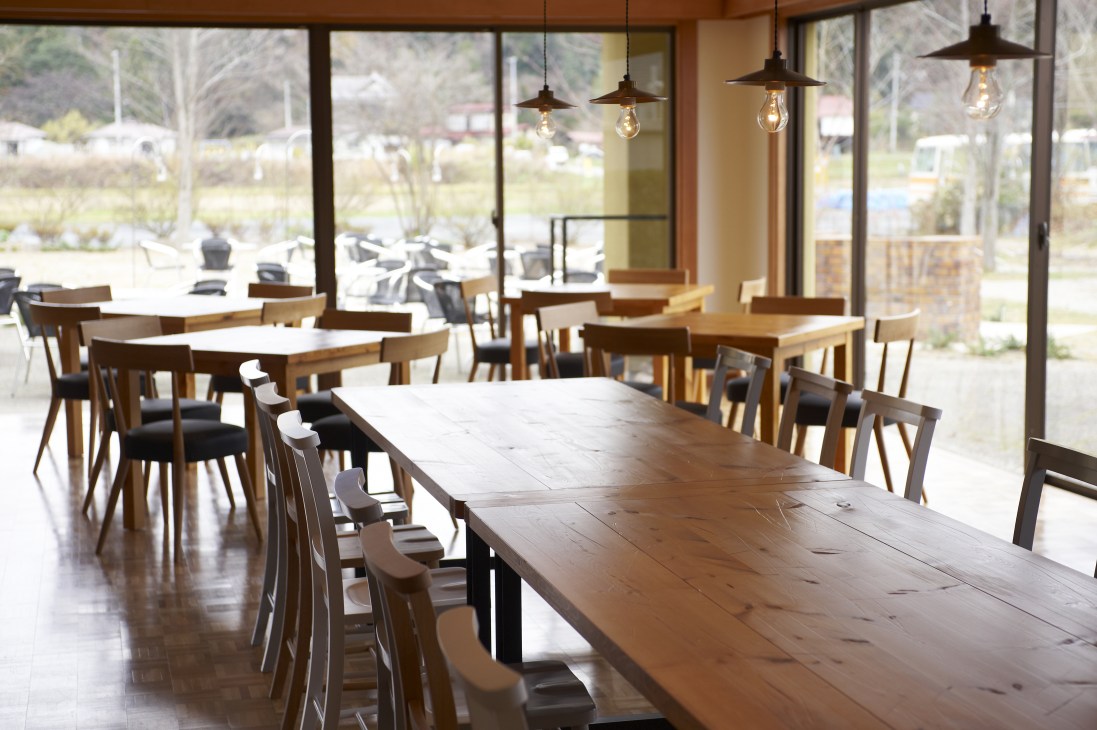 Bright dining room with wooden tables, chairs, and pendant lights overlooking countryside.