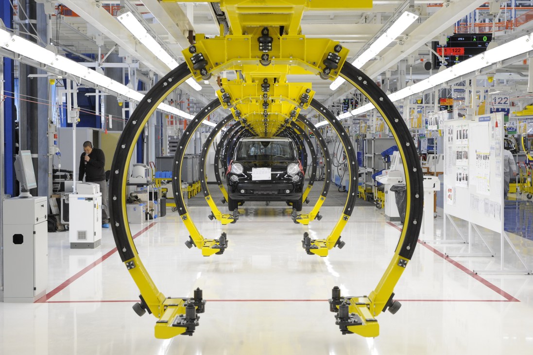 Automated car assembly line at Zastava's factory in Serbia with yellow robotic arms working on a black vehicle.