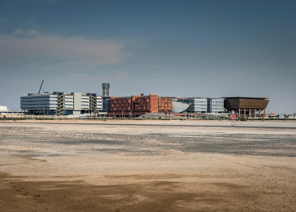 Masdar City's modernist buildings with terracotta and metallic facades viewed from barren desert landscape.