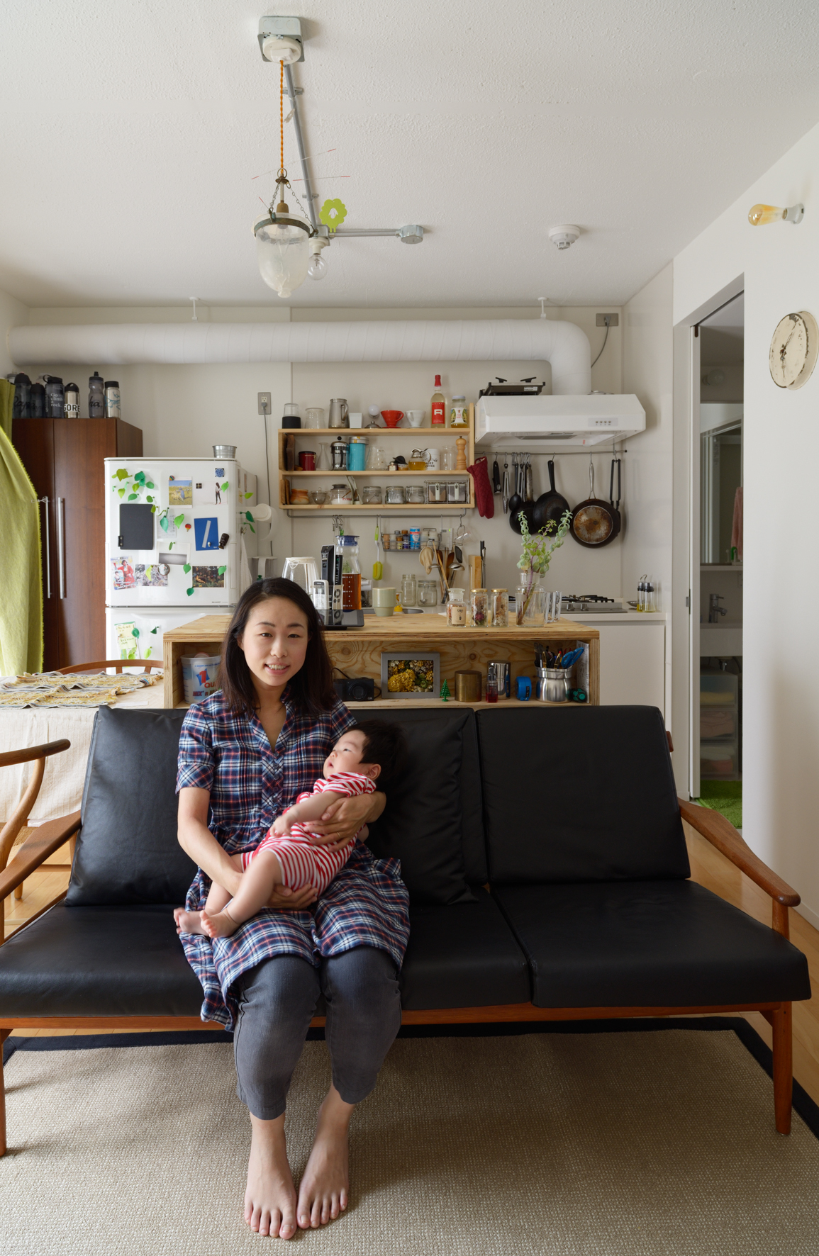 Mari Hiraiwa sits on a black sofa holding her infant daughter Sei in a renovated Tokyo apartment.
