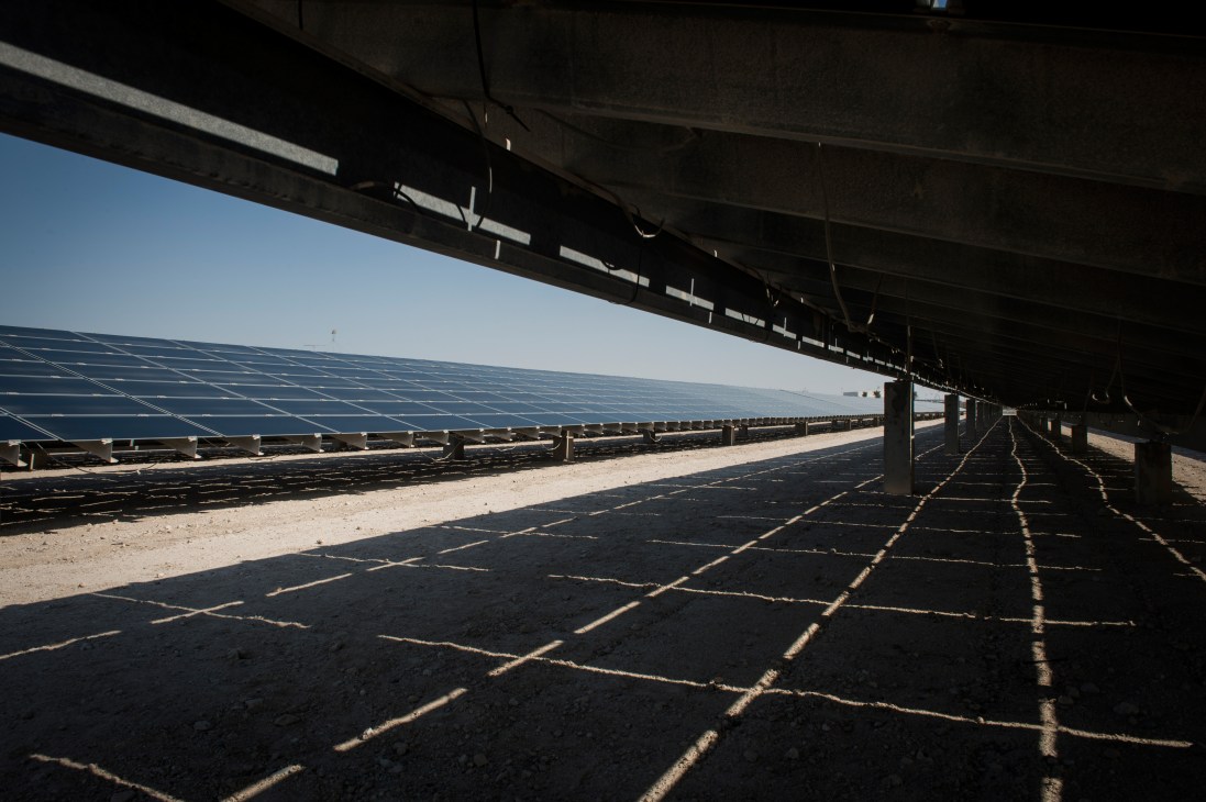 Solar photovoltaic panels installed in rows across desert landscape under metal structural framework.