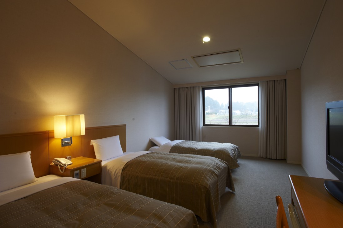 Hotel room with three beds, warm lighting, and large windows overlooking countryside landscape.
