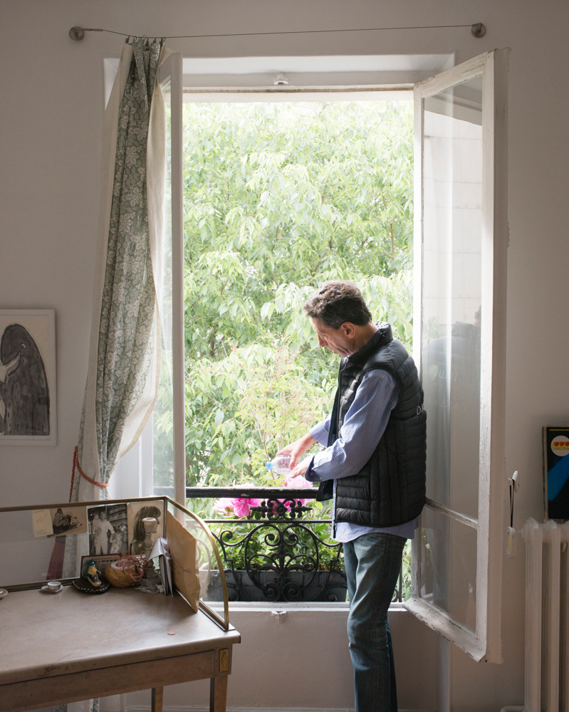 Man ironing clothes on a balcony overlooking green foliage.