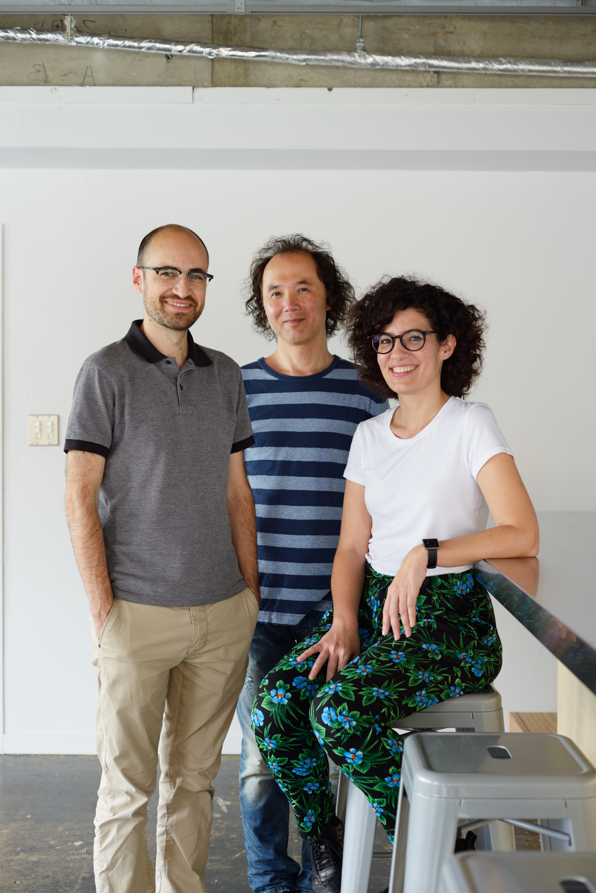 Three employees at design firm Designit stand in a bright office space with exposed ceiling beams.