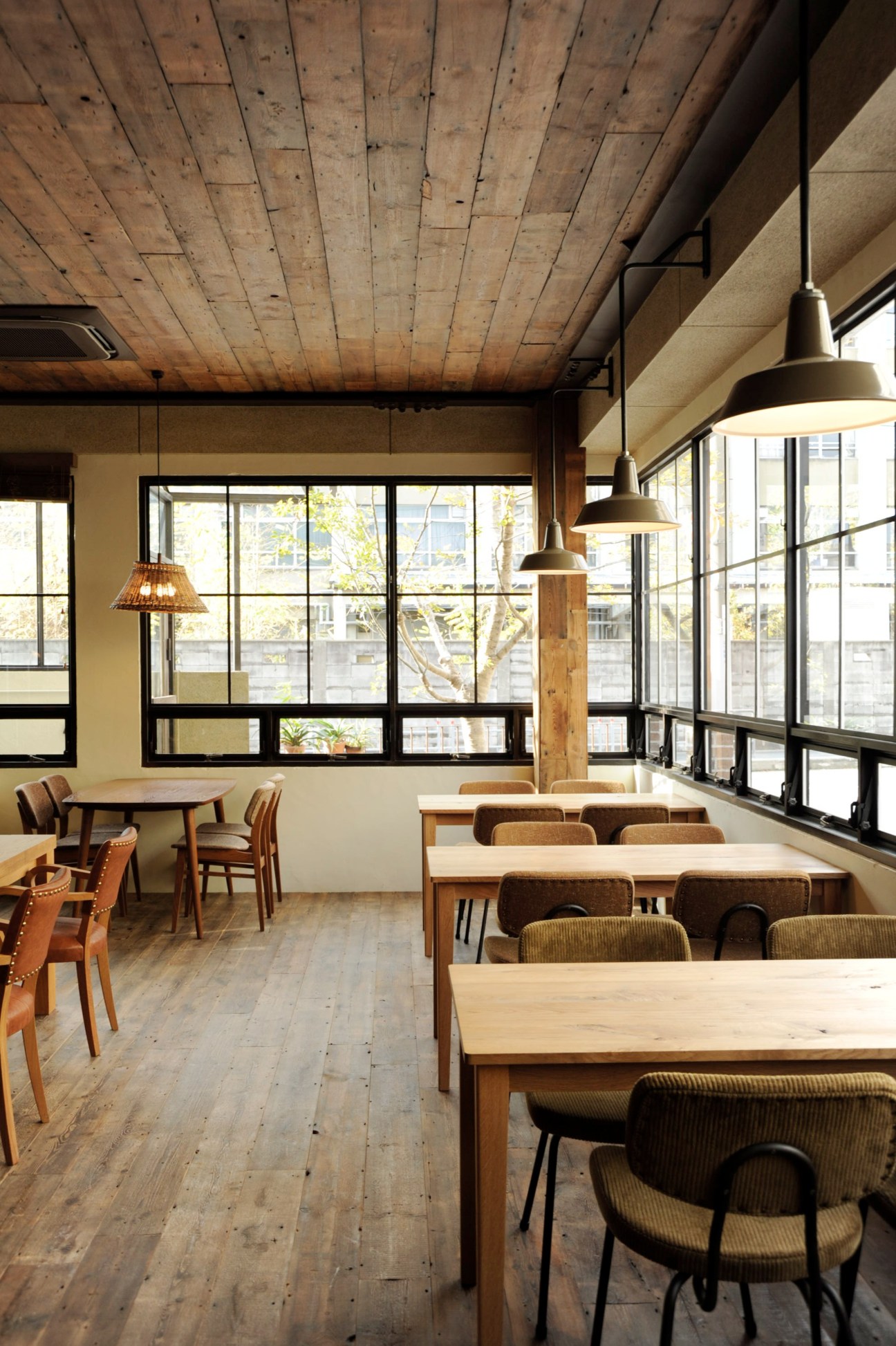 Bird café interior with wooden tables, chairs, and pendant lights under exposed wood ceiling.