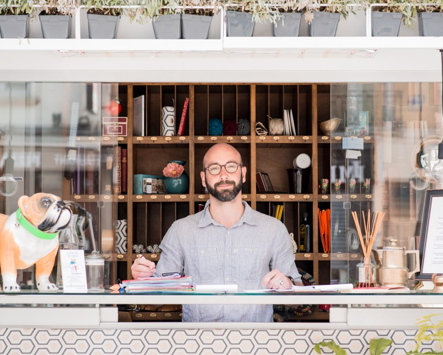 Sebastien Juin stands at the counter of Lulu Dans ma Rue's kiosk in Paris, wearing a light blue shirt.