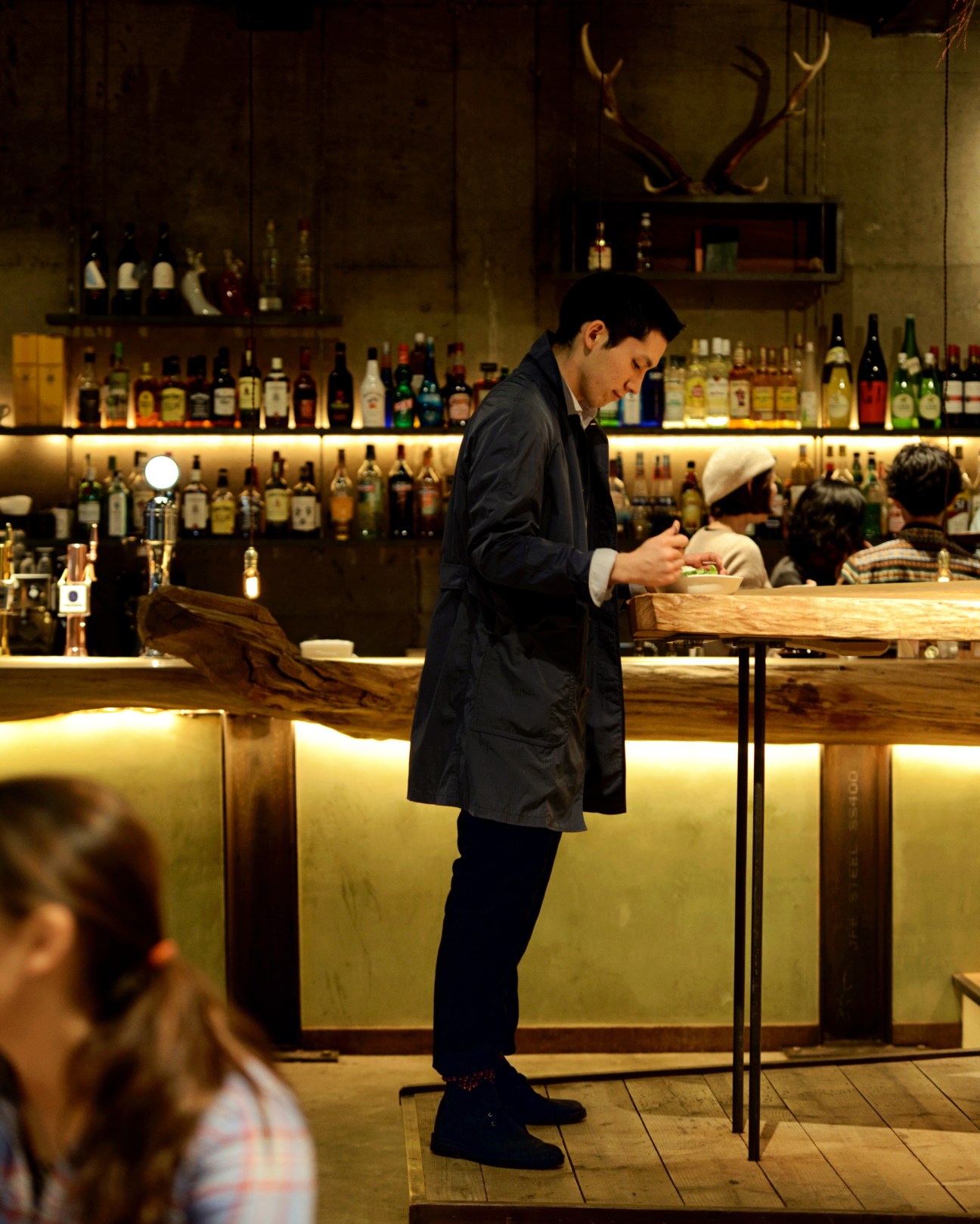 Man in black Gucci coat and Boss shirt standing at a bar counter eating ga-prao rice.