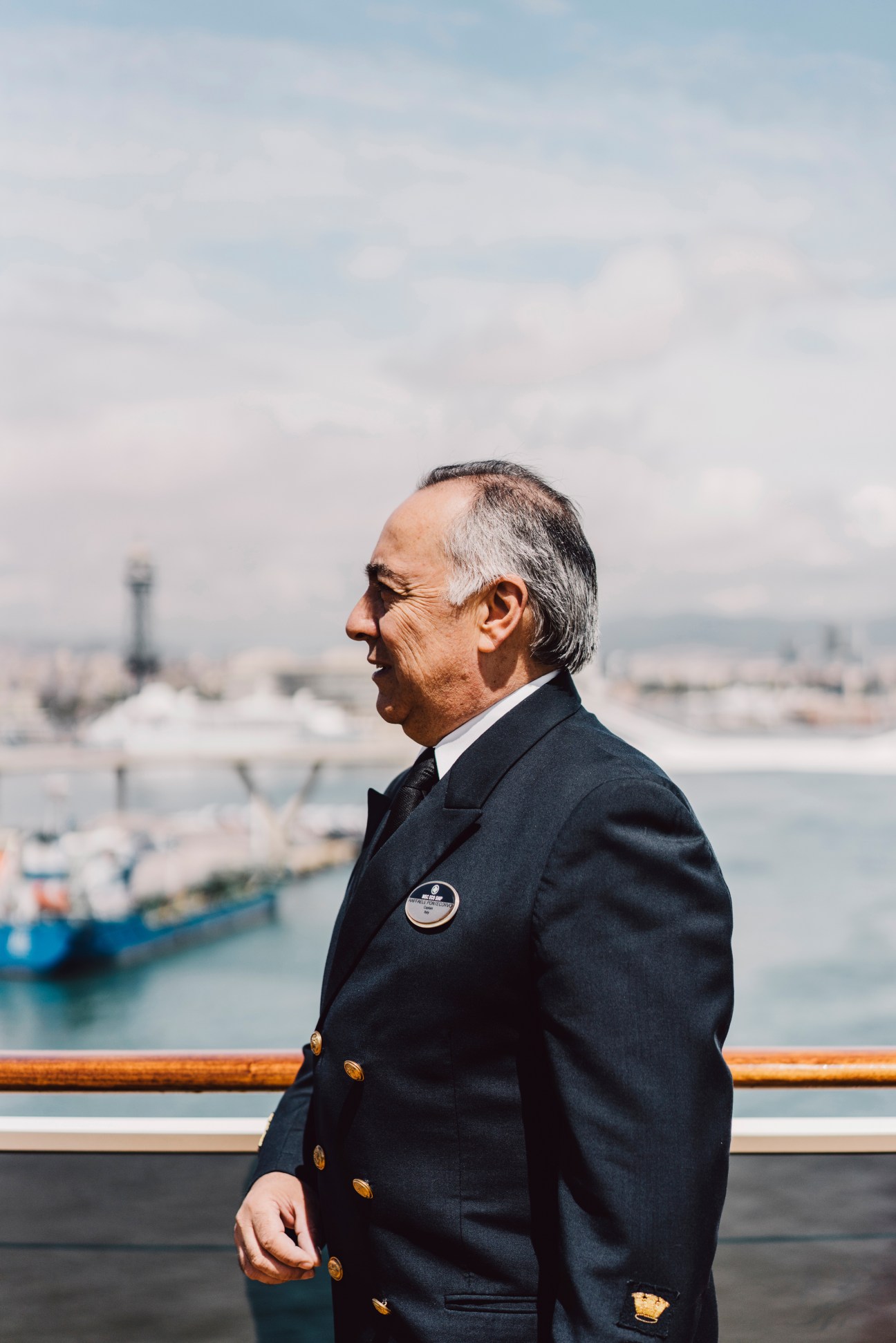 Captain Raffaele Pontecorvo in formal navy uniform with gold buttons stands on deck overlooking a port city.