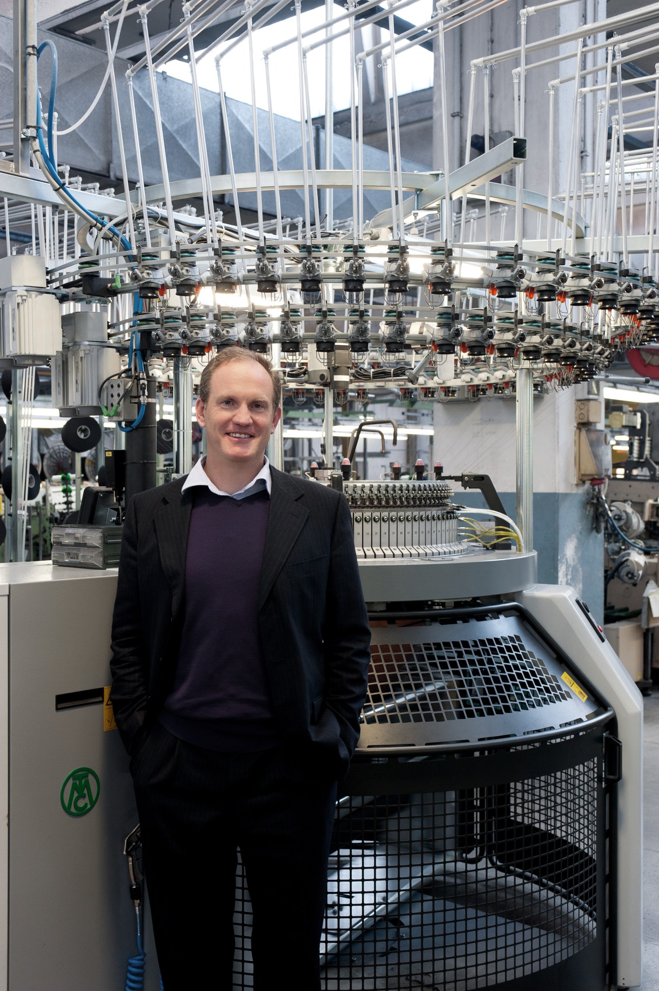 Man in business casual attire standing in front of industrial textile manufacturing machinery
