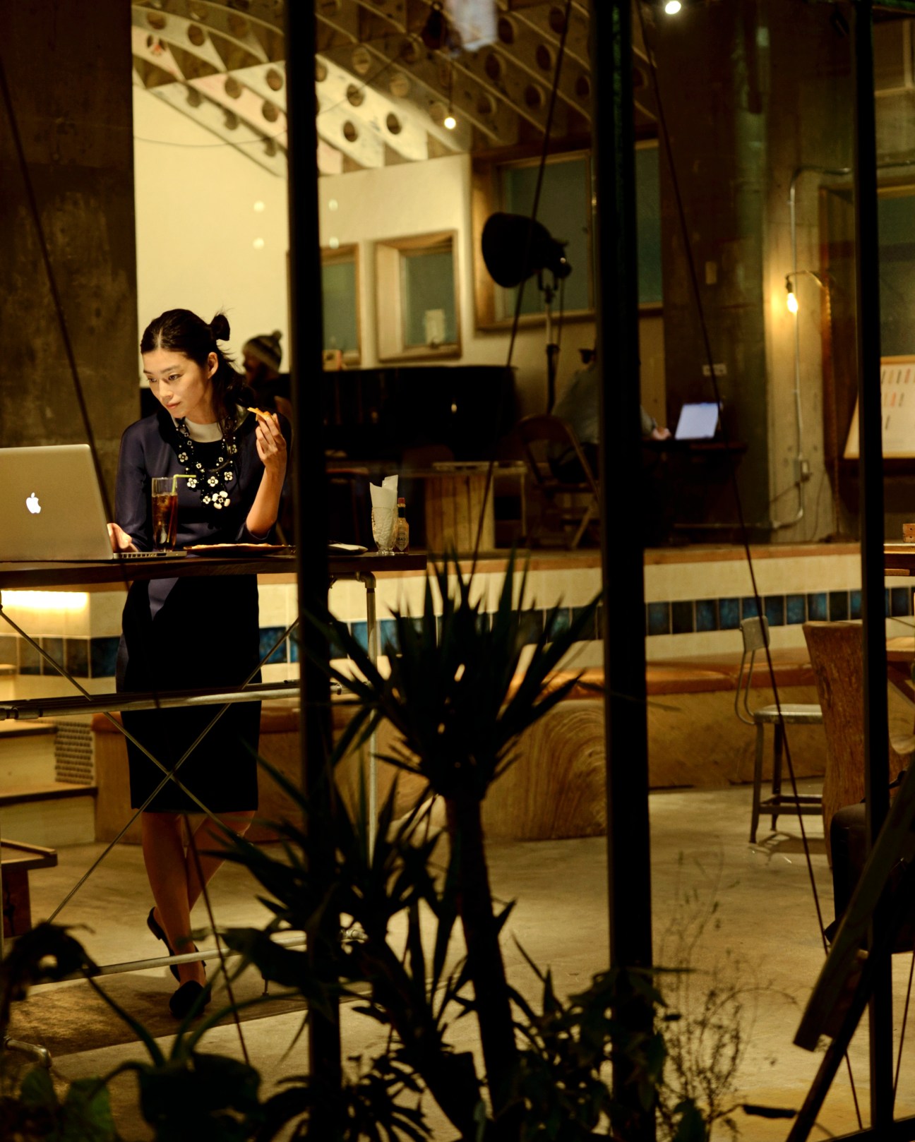Woman in Prada dress and necklace working at a counter in a Tokyo café at night.