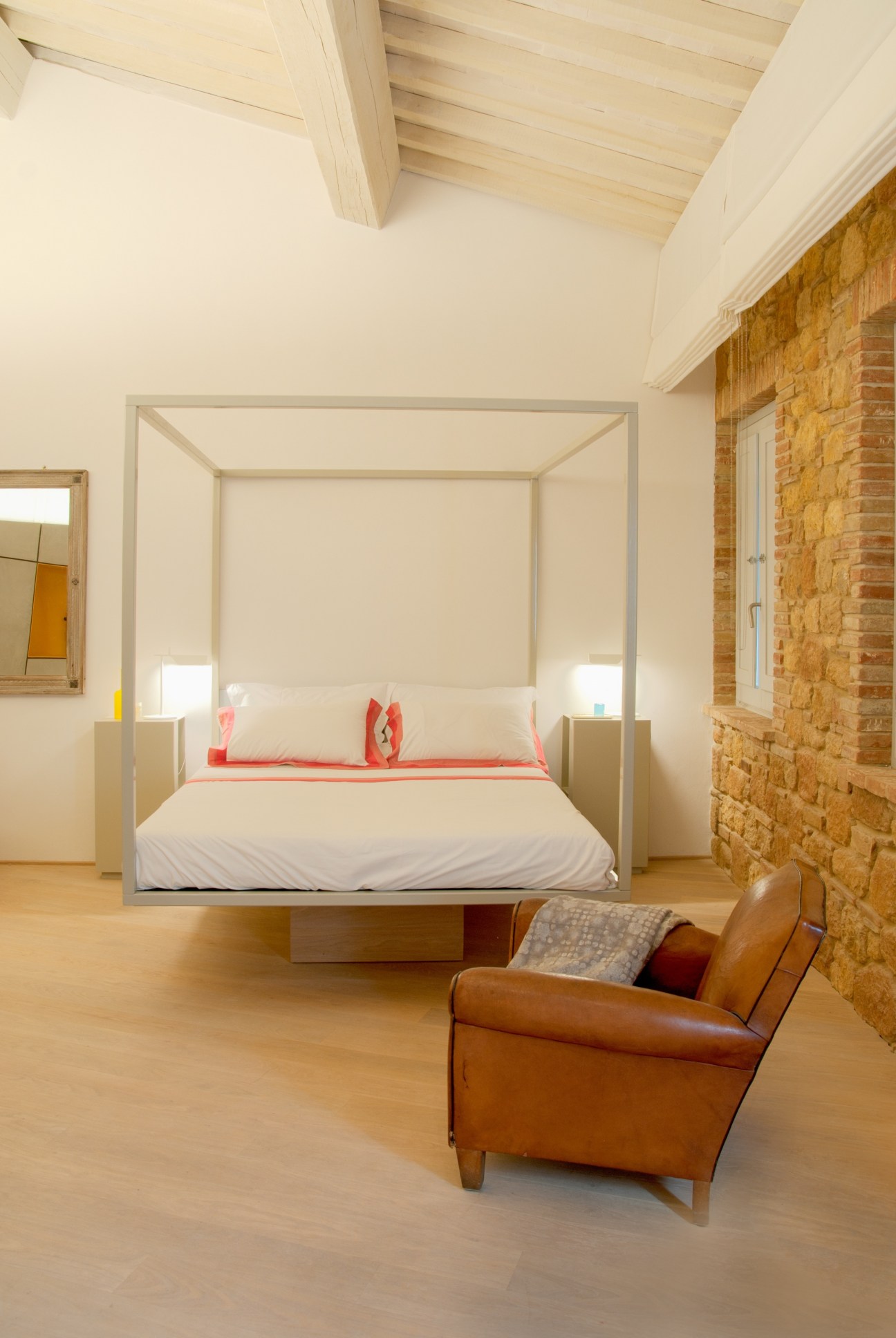 Minimalist bedroom at La Bandita with a four-poster bed, exposed brick wall, and leather armchair.