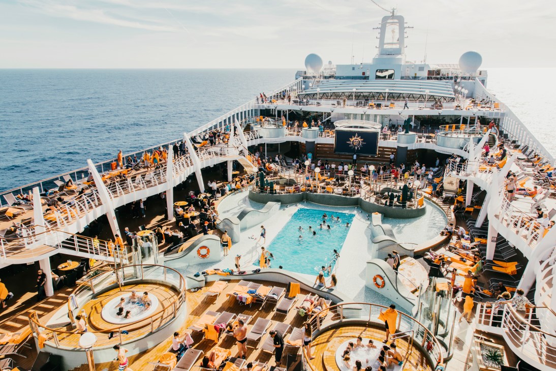 Aerial view of MSC Preziosa's top deck with swimming pool, loungers, and passengers on multiple levels at sea.