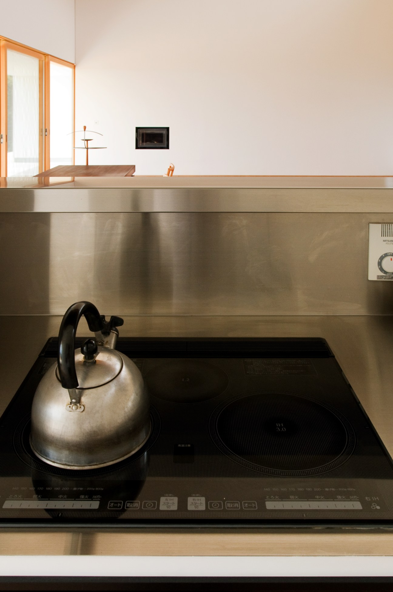 Minimalist kitchen with stainless steel countertop, induction cooktop, and metal kettle under pendant lighting.