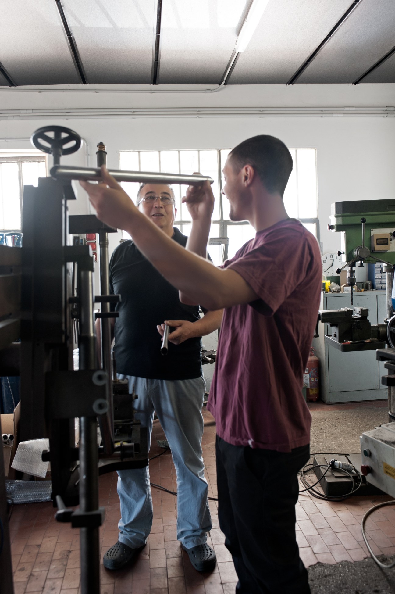 Two men in a bicycle frame workshop examining a steel tube together and laughing.