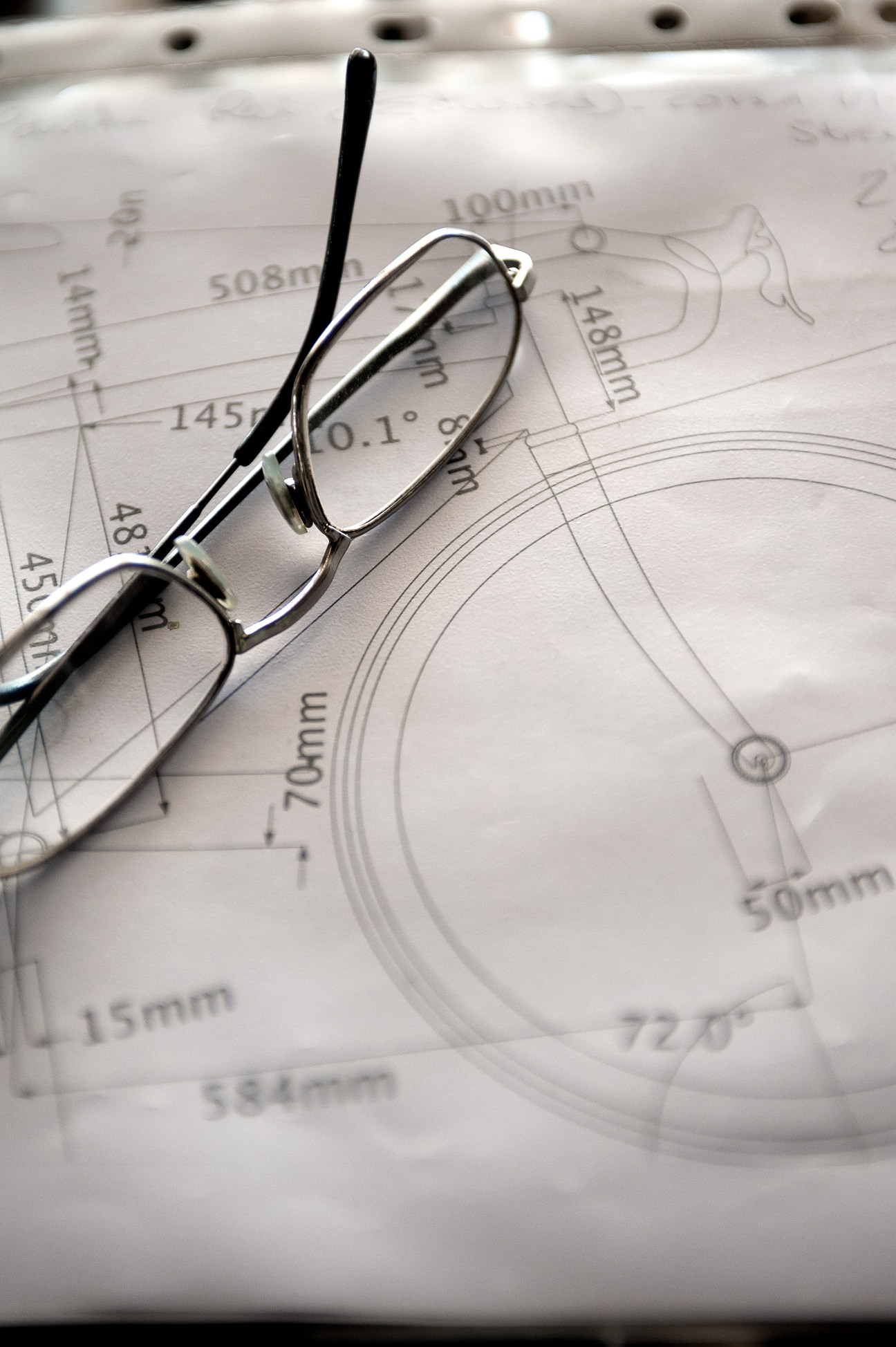 Eyeglasses resting on technical bicycle frame design blueprints with measurements and specifications.