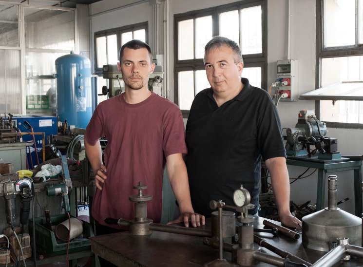Tiziano Zullo and Mattia Paganotti stand together at a workbench in their bicycle frame-building workshop in Verona.