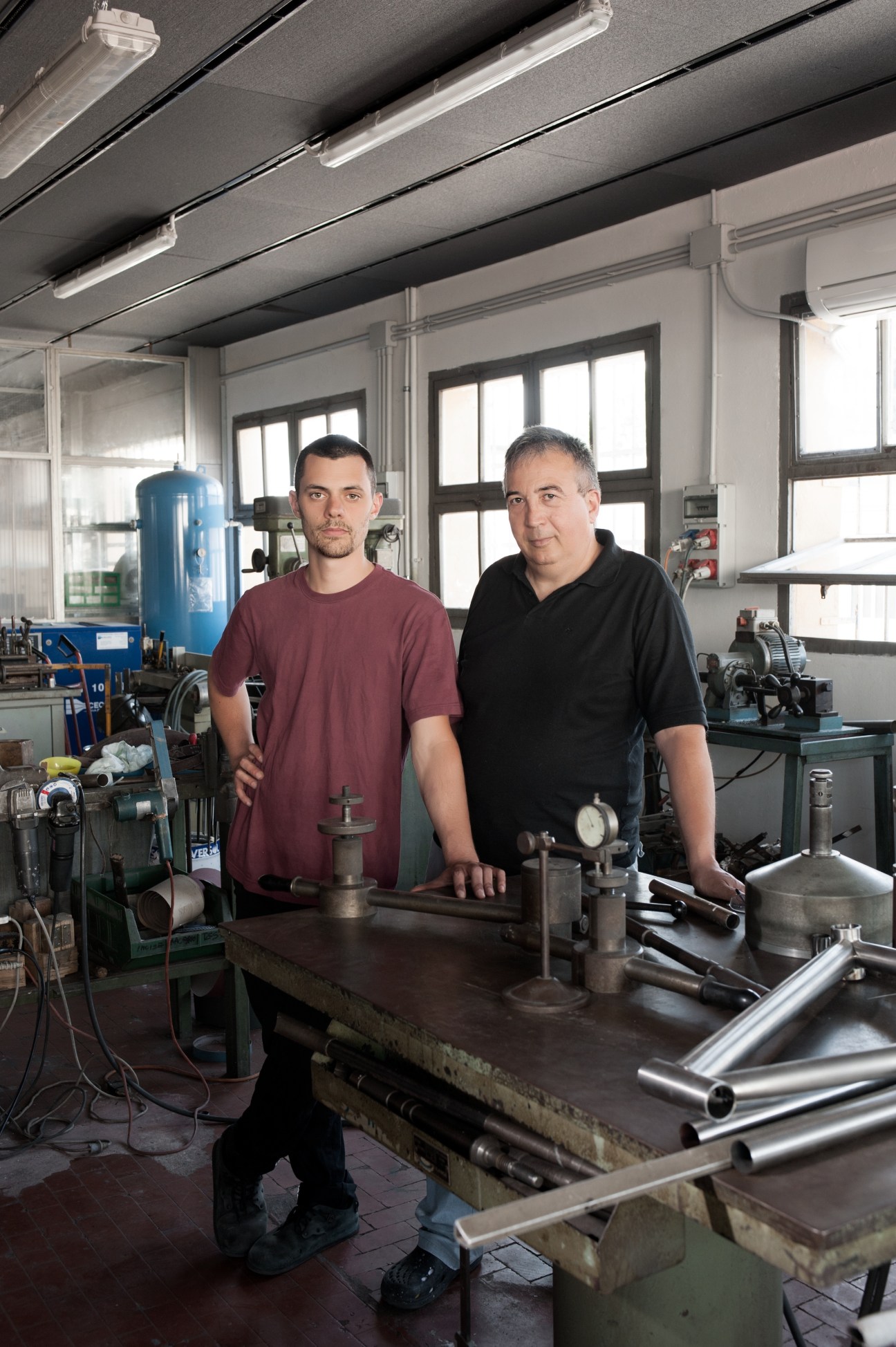 Tiziano Zullo and Mattia Paganotti stand together at a workbench in their bicycle frame-building workshop in Verona.