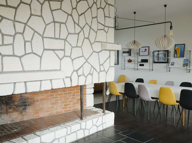 Modern interior with geometric wall pattern, pendant lights, and colorful mid-century chairs at a dining table.