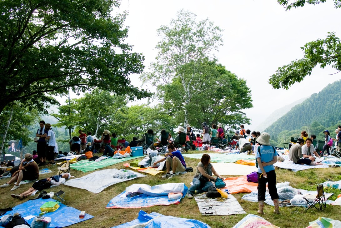 Festival attendees relax on colorful blankets between performances at Fuji Rock, with forested mountains visible in the background.
