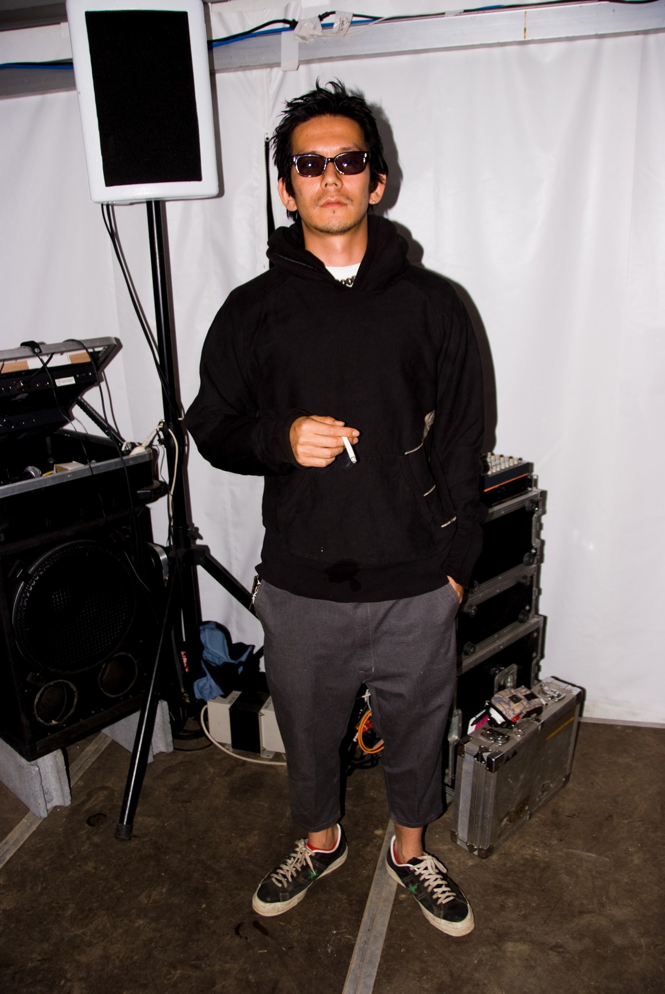 Man in black hoodie and sunglasses standing backstage with musical equipment