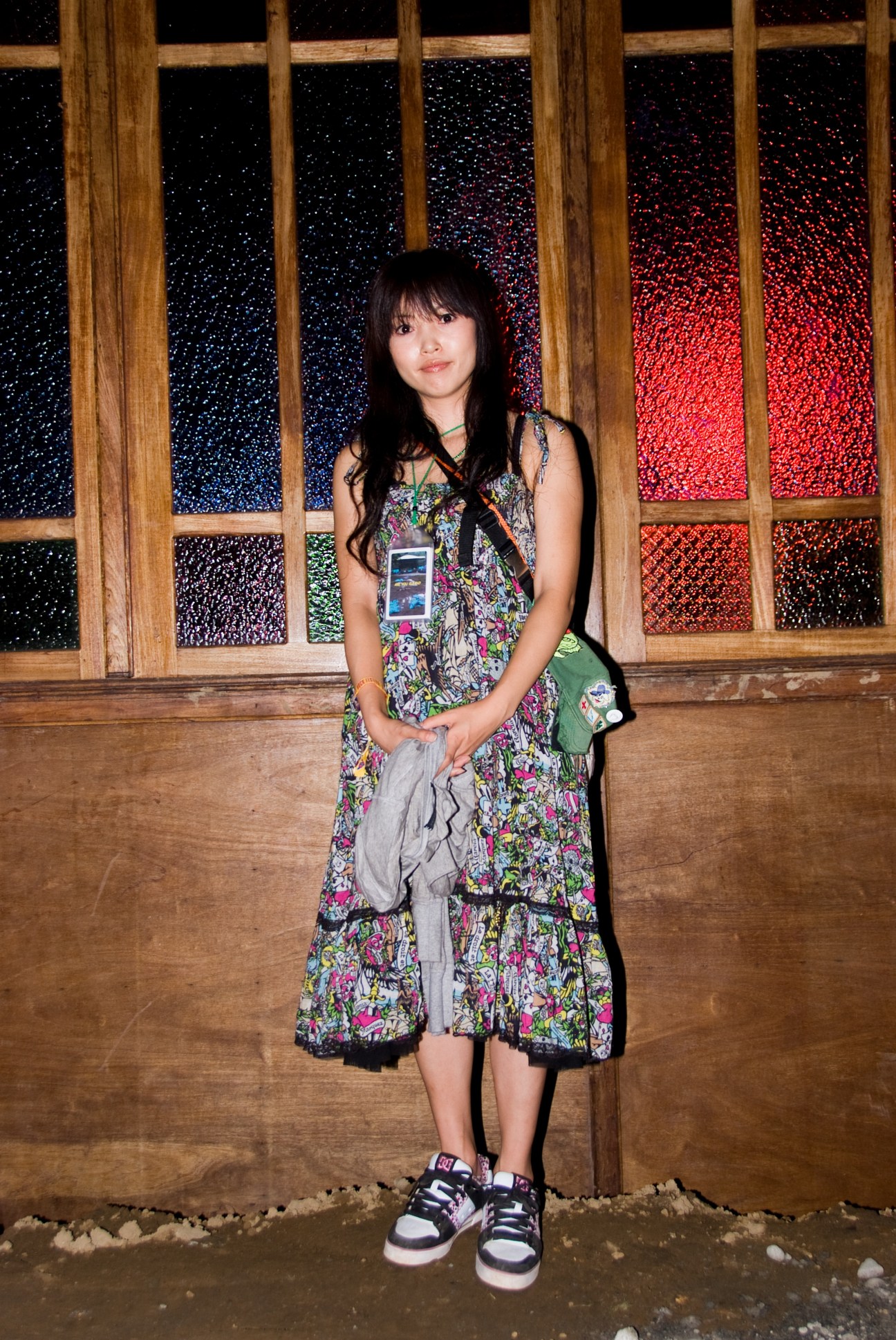 Young woman in floral dress standing against illuminated window display at Fuji Rock Festival.