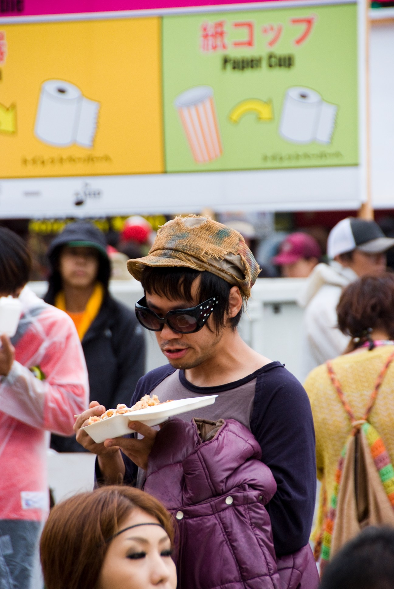 Festival-goer wearing sunglasses and brown cap holds food at Fuji Rock's food village.