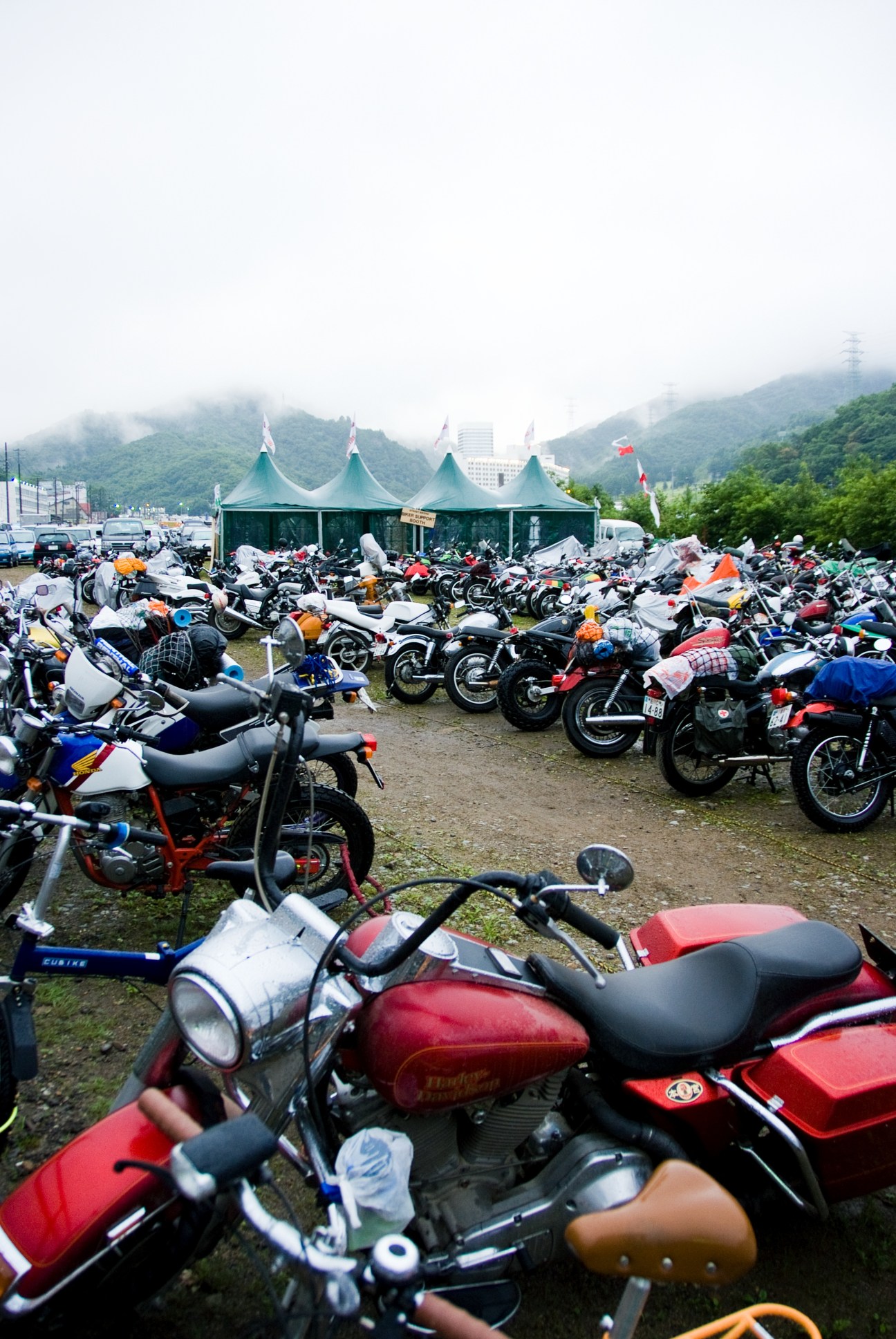 Motorcycles parked in misty field at Fuji Rock Festival with green tent and mountains in background.