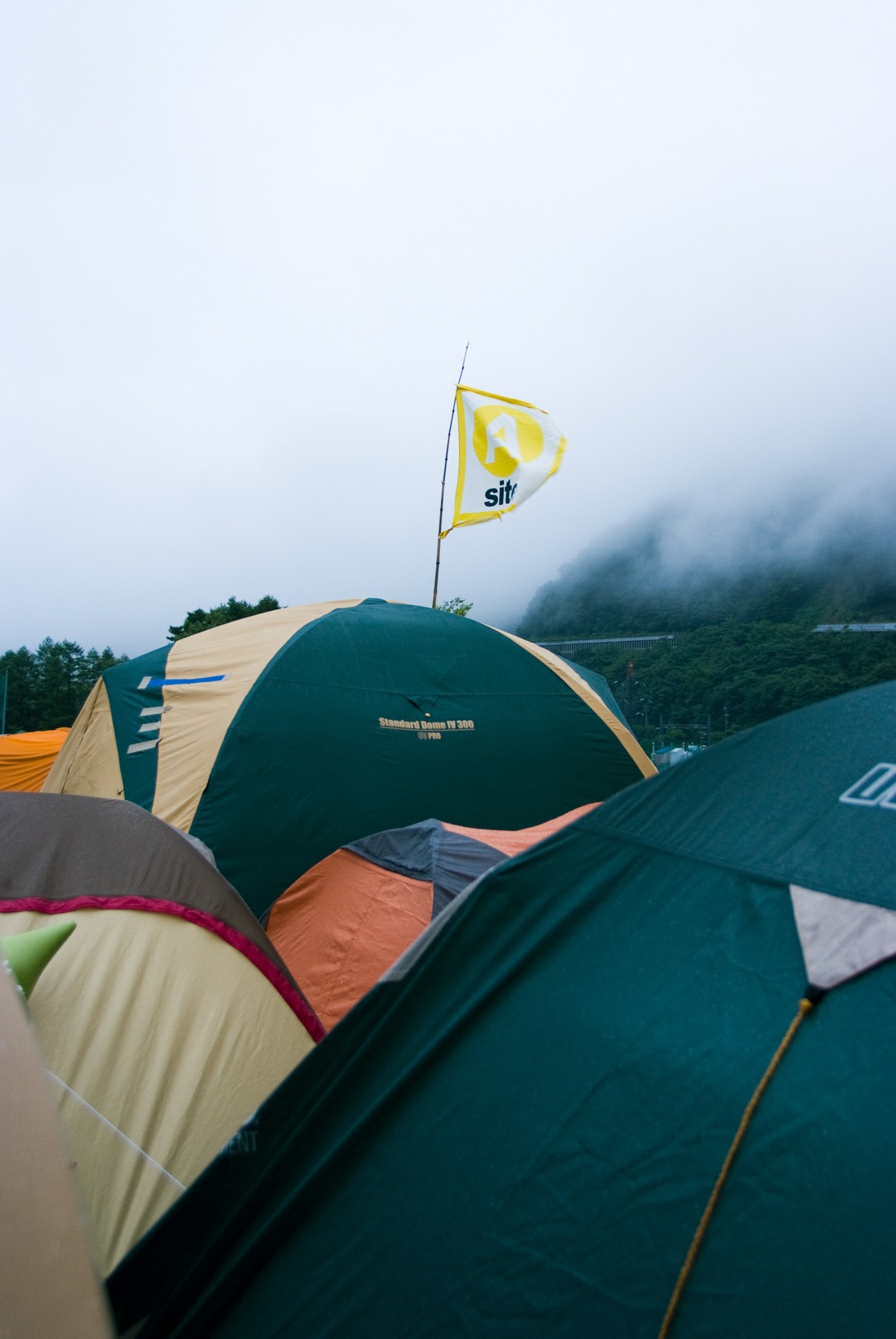 Camping tents with a yellow flag at Fuji Rock Festival in mountainous terrain.
