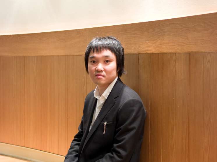 Hiroaki Narita, founder of Connect furniture auction house, sitting on a wooden bench against a wood-paneled wall.