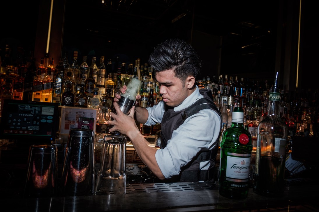Bartender in white shirt and black bulletproof vest mixing a drink behind a well-stocked bar.