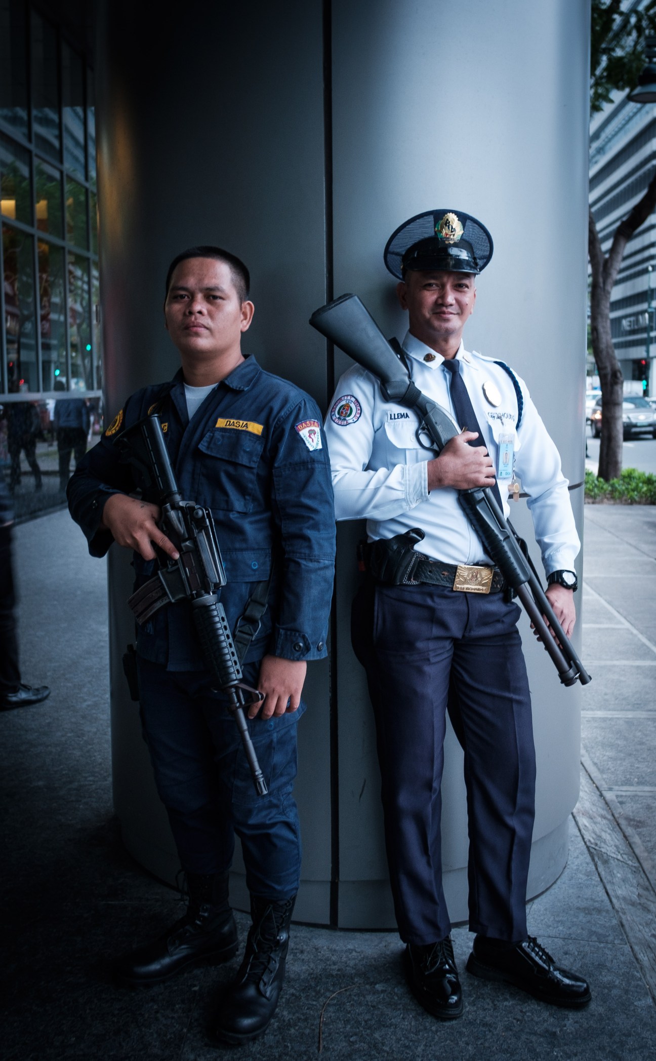 Two armed guards in uniform stand outside a modern building in Manila.