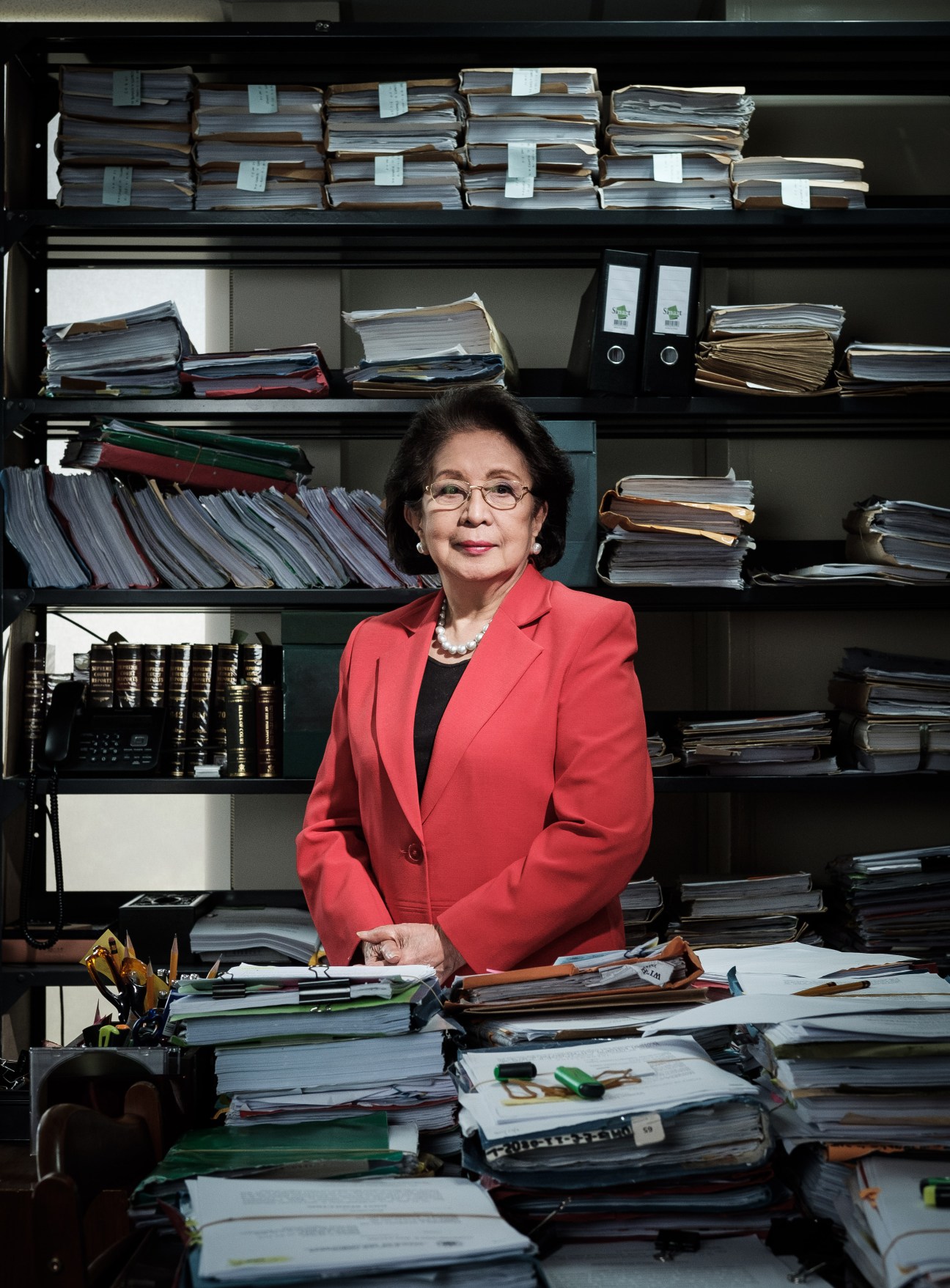 Ombudsman Conchita Carpio-Morales at her desk surrounded by stacked files and folders.