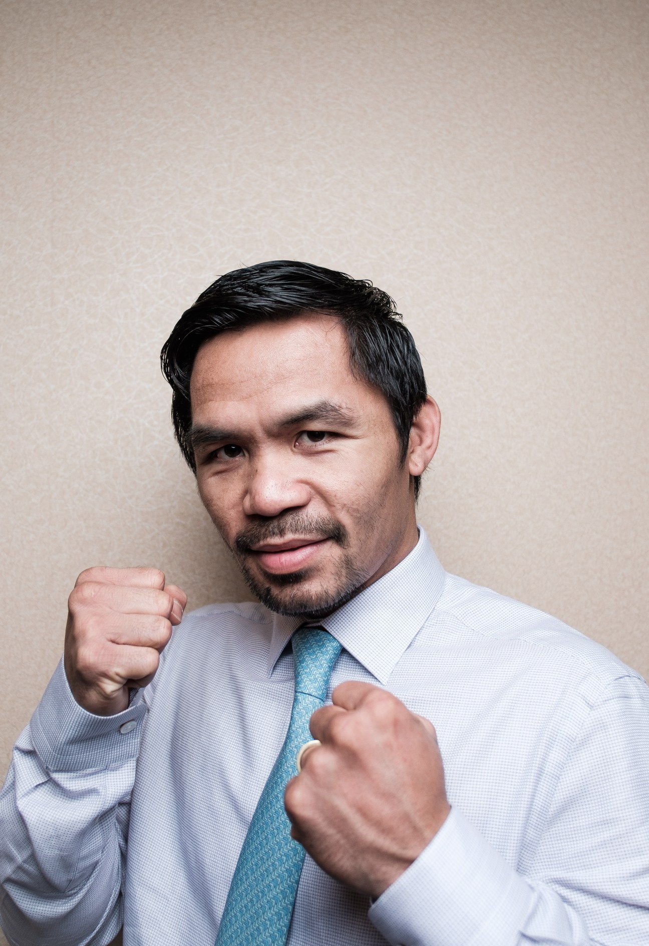 Senator Manny Pacquiao in a light blue shirt and blue tie, posing with both fists raised in a boxing stance.